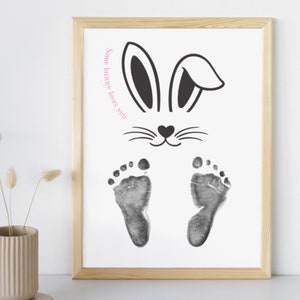 May include: A white framed print with a black bunny rabbit silhouette and the text "Some bunny loves you" in pink. The bunny has two black foot prints below it.