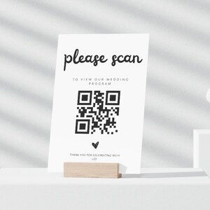 Peut inclure: Carte blanche avec du texte noir qui dit "please scan" et "to view our wedding program". Un code QR noir et blanc se trouve sous le texte. Le texte "thank you for celebrating with us" est en bas de la carte.
