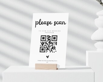 Op de afbeelding: Witte kaart met zwarte tekst die "please scan" en "to view our wedding program" zegt. Onder de tekst staat een zwart-witte QR-code. De tekst "thank you for celebrating with us" staat onderaan de kaart.