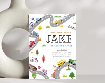 May include: A birthday invitation for a boy named Jake turning three. The invitation features a winding road with various vehicles, including a bus, car, ambulance, and airplane. The text "BEEP. HONK. VROOM. JAKE IS TURNING THREE" is printed in black and blue on a white background.