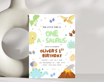 May include: A white invitation card with a dinosaur theme. The text reads "Our Little Dino is One A-Saurus!" and "Oliver's 1st Birthday." The card features cartoon dinosaurs, footprints, and a volcano illustration.