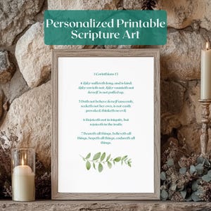 May include: A framed print with the text "Personalized Printable Scripture Art" at the top. The print features a passage from 1 Corinthians 13, with a sprig of green leaves at the bottom. A lit candle is visible on the left.