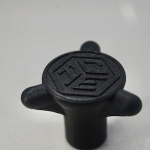 Puede incluir: Una perilla de plástico negro con tres puntas y un diseño hexagonal que presenta el texto "703" en el centro.