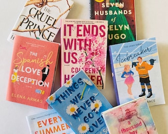 May include: A collection of miniature books with colorful covers. Titles include "The Cruel Prince," "It Ends With Us," "The Spanish Love Deception," and "Every Summer After." The books are arranged on a white surface.