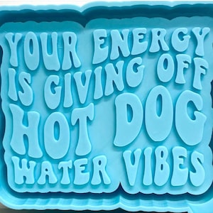 May include: A blue silicone mold with the text "Your energy is giving off hot dog water vibes" in a retro font.
