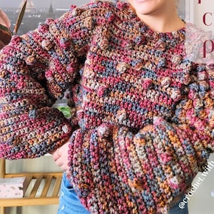 May include: A multi-coloured crochet pullover with bell sleeves and a textured bobble stitch design. The text "aspen pullover crochet pattern" is displayed on the image. The colour palette includes shades of pink, blue, brown, and yellow.