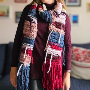 May include: A colorful crocheted scarf with long fringe in shades of pink, red, blue, and white.