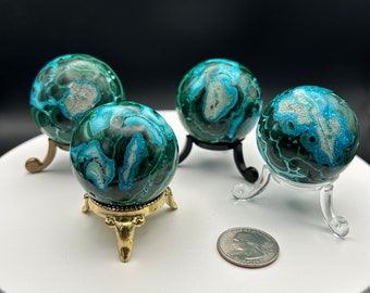 May include: Four green and blue malachite spheres on decorative stands. The spheres are polished and have a swirling pattern. One sphere is on a gold stand, two are on black stands, and one is on a clear plastic stand.