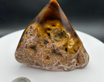 May include: A pyramid-shaped, polished agate crystal with brown, white, and black markings. The crystal is translucent and has a smooth, polished surface.