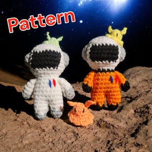 以下が含まれることがあります： 宇宙飛行士と宇宙人のアミグルミのおもちゃを作るための編み図です。このパターンには、白とオレンジの2人の宇宙飛行士と、緑とオレンジの2人の宇宙人を作り上げるための指示が含まれています。宇宙飛行士は、月の表面のような茶色の表面に立っています。
