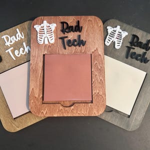 Könnte beinhalten: Drei Holzrahmen mit abgerundeten Ecken, jeweils mit einem Ausschnitt für einen quadratischen Einsatz. Die Rahmen sind in Braun-, Grau- und Beigetönen gehalten. Jeder Rahmen trägt die Worte "Rad Tech" und ein Rippenkorb-Design.