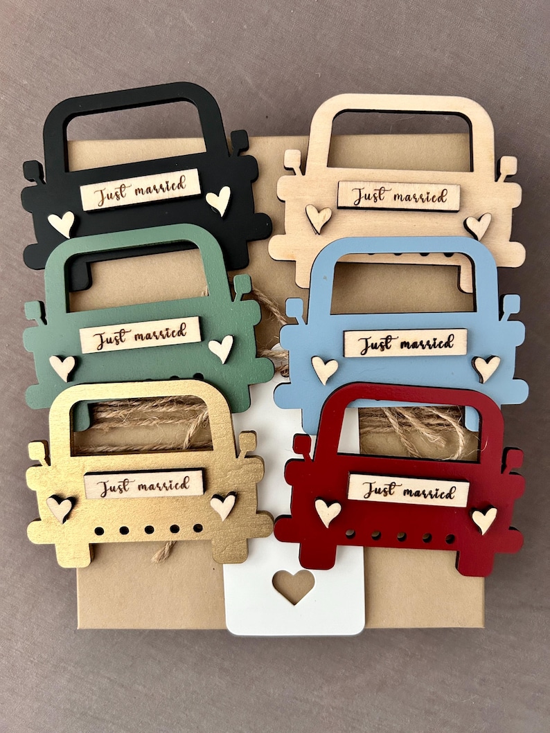 May include: Six wooden truck ornaments in different colors, including black, brown, green, blue, gold, and red. Each truck has a "Just married" sign and two small hearts.