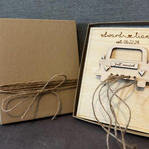May include: A wooden box with a brown paper lid tied with twine. The box contains a wooden card with a car design and the text "Edward & Lian est. 06.22.24 Just married".