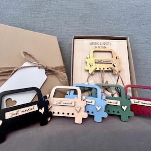 May include: Six wooden car ornaments with the words "Just Married" on them. The cars are painted in different colors: black, blue, green, red, and gold. The cars are arranged in a row on a wooden surface. The text "Wayne & Kristy 06.08.2024" is on the surface.