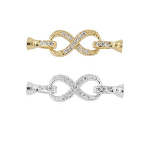 May include: Two infinity symbol clasps, one gold and one silver, with clear cubic zirconia stones. Both clasps have a small loop on one end for attaching to a chain or bracelet.