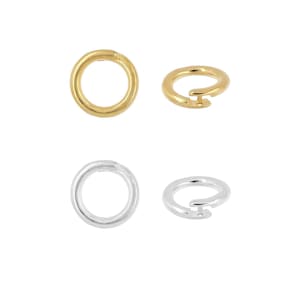 May include: Four round clasps, two in gold and two in silver, are displayed against a white background. The clasps are open, showing their circular shape and the mechanism for closure. The gold clasps have a shiny finish, while the silver ones appear polished.