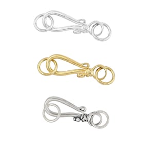 May include: Three metal clasp closures in silver and gold tones. Each clasp features a hook design with a decorative element near the center and two circular loops. The clasps are designed for jewelry making.