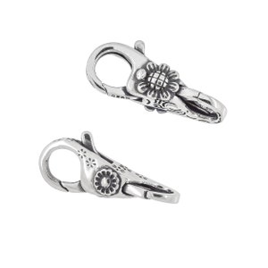 May include: Two silver-toned clasps with floral designs. Each clasp has a loop and a hook. The clasps are detailed with intricate floral patterns.