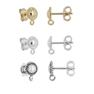 May include: Close-up of six stud earrings in gold and silver. Each earring features a round, textured design with a small loop for attaching charms or other embellishments. The earrings are displayed against a white background.