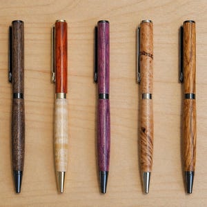 May include: Five wooden pens with different wood grains and colours, including dark brown, reddish-orange, purple, light brown, and patterned brown. Each pen has a black or silver clip and tip, highlighting the natural beauty of the wood.