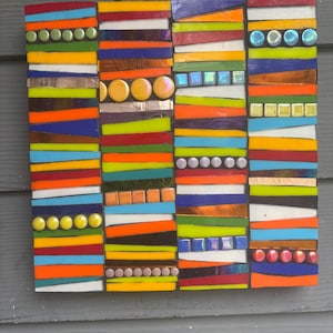 May include: A colorful mosaic artwork composed of rectangular panels. Each panel features horizontal stripes in various colors, including orange, blue, green, and yellow. Decorative glass beads and tiles are interspersed throughout the design, adding texture and dimension to the piece.