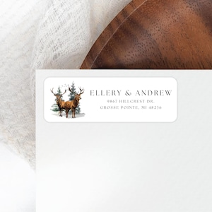 May include: A white rectangular return address label with a watercolor illustration of two brown deer standing in a snowy forest. The text "ELLERY & ANDREW", "9867 HILLCREST DR.", and "GROSSE POINTE, MI 48236" is printed in black.