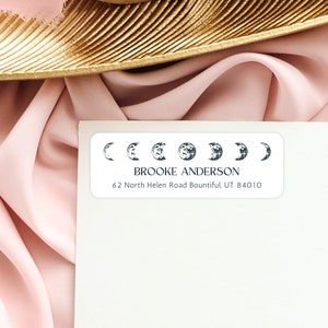 May include: White return address label with a moon phase design. The label reads "BROOKE ANDERSON" and "62 North Helen Road Bountiful, UT 84010".