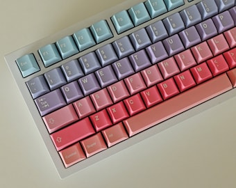 May include: A white mechanical keyboard with pastel-colored keycaps. The keycaps are a gradient of blue, purple, pink, and red. The keyboard has a standard layout with function keys, number keys, and letter keys. The keyboard also has a space bar, control keys, and a super key.