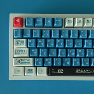 Op de afbeelding: Een wit en blauw mechanisch toetsenbord met Japanse karakters op de toetsen. Het toetsenbord heeft een zwarte balk met de tekst "新世紀エヴァンゲリオン" (Shin Seiki Evangelion) erop. Het toetsenbord heeft een rode toets met een wit symbool erop.