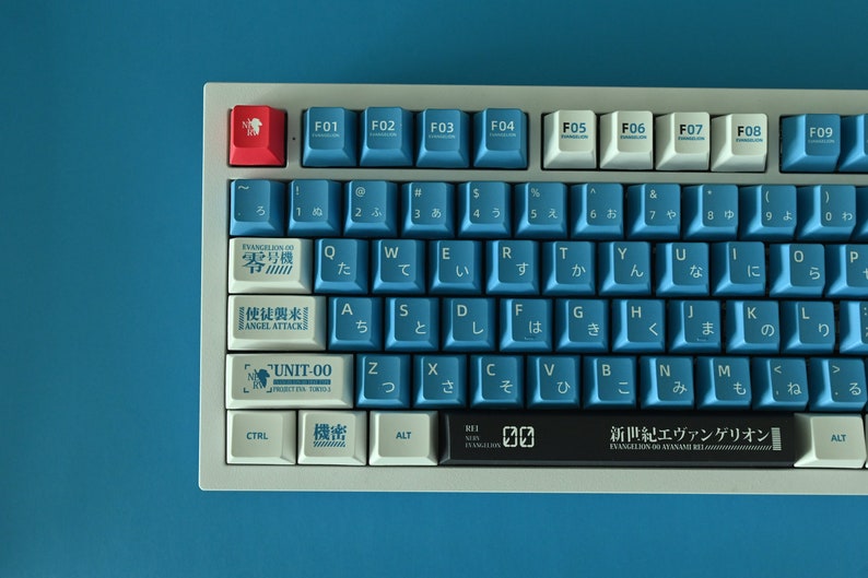 Op de afbeelding: Een wit en blauw mechanisch toetsenbord met Japanse karakters op de toetsen. Het toetsenbord heeft een zwarte balk met de tekst "新世紀エヴァンゲリオン" (Shin Seiki Evangelion) erop. Het toetsenbord heeft een rode toets met een wit symbool erop.