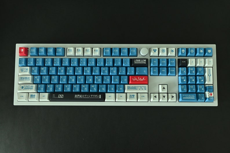 Op de afbeelding: Een wit en grijs mechanisch toetsenbord met blauwe en rode toetsen. Het toetsenbord heeft een Japanse lay-out met de tekst "新世紀エヴァンゲリオン" gedrukt op de spatiebalk.