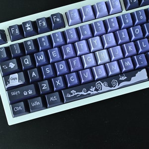 May include: A white mechanical keyboard with a gradient of purple and blue keys. The keys have various Halloween-themed symbols and graphics, including ghosts, tombstones, and spiderwebs.