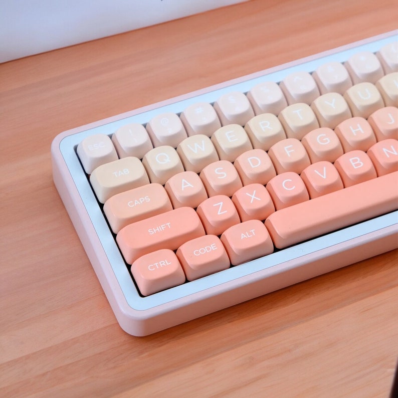 K&ouml;nnte beinhalten: Eine rosa und wei&szlig;e Tastatur mit pastellorangen Tasten. Die Tasten haben wei&szlig;e Beschriftung und beinhalten die Standardtasten wie TAB, CAPS, SHIFT, CTRL, ALT und CODE.