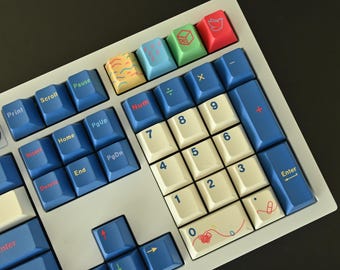 Peut inclure: Gros plan sur un clavier mécanique avec des touches blanches, bleues et crème. Les touches sont disposées selon une disposition standard, avec un pavé numérique et des touches de fonction. Certaines touches ont des motifs colorés.