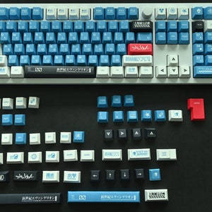 Op de afbeelding: Een wit mechanisch toetsenbord met blauwe en witte toetsen. De toetsen hebben Japanse karakters en symbolen. Er zijn ook verschillende extra toetsen in blauw, wit, zwart en rood.