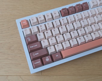 May include: A white mechanical keyboard with brown and pink keycaps. The keyboard has a light blue frame and a peach-colored space bar.
