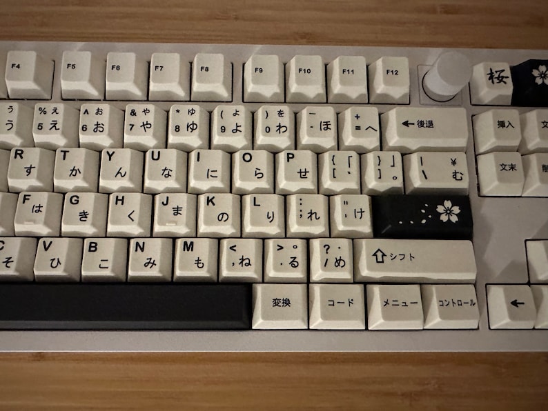 K&ouml;nnte beinhalten: Eine wei&szlig;e Tastatur mit schwarzen Tasten und japanischen Zeichen. Die Tastatur hat eine schwarze Leertaste und eine schwarze Taste mit einem wei&szlig;en Blumendesign.