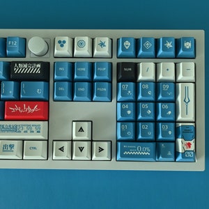 Op de afbeelding: Een wit mechanisch toetsenbord met blauwe en rode toetsen. De toetsen hebben Japanse karakters en symbolen. Het toetsenbord heeft een numeriek toetsenblok en pijltjestoetsen.