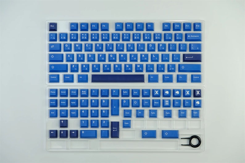 K&ouml;nnte beinhalten: Eine geteilte mechanische Tastatur mit blauen Tastenkappen und japanischen Schriftzeichen. Die Tastenkappen sind in einem leuchtenden Blau gehalten, mit wei&szlig;er Beschriftung. Die Tastatur befindet sich in einem transparenten Kunststoffgeh&auml;use, und ein Keycap-Abzieher ist enthalten.