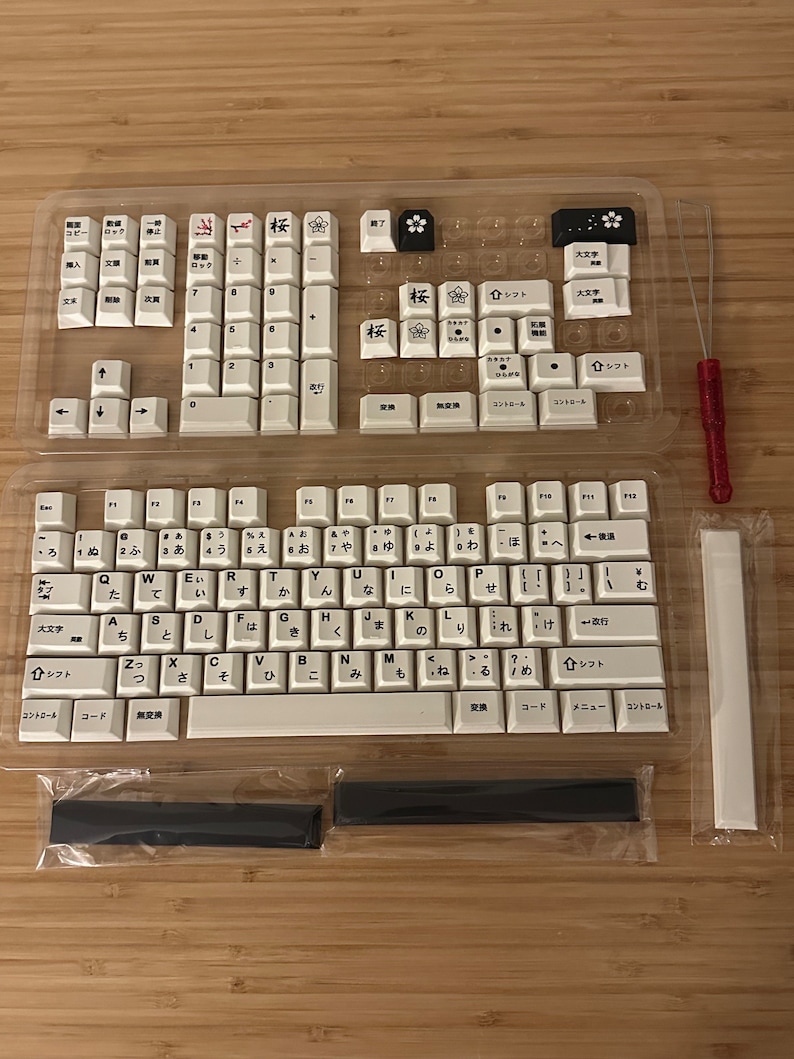 K&ouml;nnte beinhalten: Eine wei&szlig;e mechanische Tastatur mit japanischen Tastenkappen. Die Tastatur befindet sich in einem durchsichtigen Kunststoffgeh&auml;use und enth&auml;lt einen Satz schwarzer und wei&szlig;er Tastenkappen, einen wei&szlig;en Tastenkappenzieher und zwei schwarze Stabilisatoren.