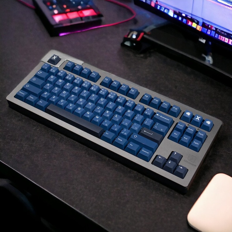 K&ouml;nnte beinhalten: Eine mechanische Tastatur mit einem dunkelgrauen Rahmen und marineblauen Tastenkappen. Die Tastatur hat ein Standardlayout mit alphanumerischen Tasten, Funktionstasten und einem Nummernblock. Die Tastenkappen haben wei&szlig;e Buchstaben und Symbole. Die Tastatur befindet sich auf einer dunklen Oberfl&auml;che.