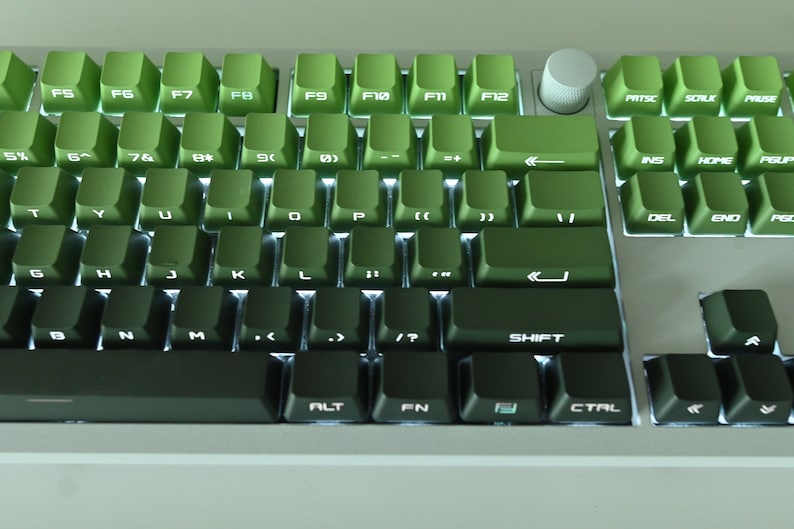 以下が含まれることがあります： キーに白い文字が書かれた緑色のメカニカルキーボード。キーボードは右側にテンキー、上部にファンクションキーの列があります。