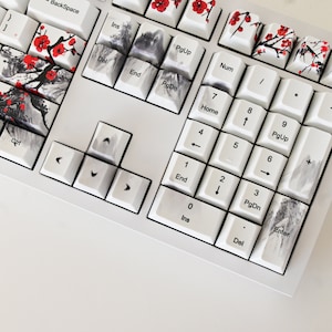 May include: A white mechanical keyboard with custom keycaps featuring a Japanese-inspired design. The keycaps have black and white ink wash designs with red accents. The keyboard has a white frame and white keys.