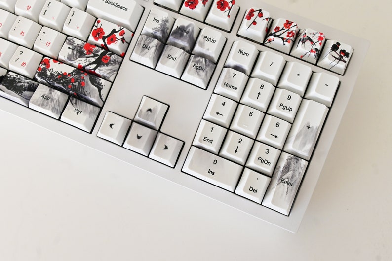 May include: A white mechanical keyboard with custom keycaps featuring a Japanese-inspired design. The keycaps have black and white ink wash designs with red accents. The keyboard has a white frame and white keys.