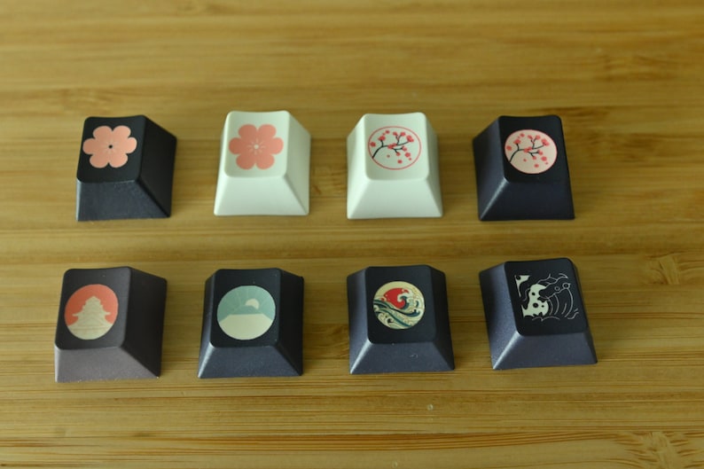 K&ouml;nnte beinhalten: Zehn Tastenkappen mit verschiedenen Designs. Die Tastenkappen sind schwarz, wei&szlig; und grau mit verschiedenen darauf gedruckten Bildern. Die Bilder beinhalten eine Blume, einen Kirschbl&uuml;tenzweig, einen Berg, eine Welle und einen Fisch.