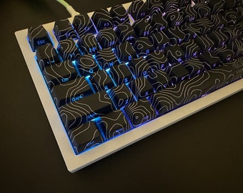 May include: A white mechanical keyboard with black keycaps featuring a topographic pattern. The keys are backlit with a blue light. The keyboard has keys labelled 'Esc', 'Tab', 'Caps', 'Shift', 'Ctrl', 'Win', 'Alt', 'F1', 'F2', 'F3', 'F4', 'F5', 'F6', 'F7', 'F8', 'F9', 'F10', 'F11', 'F12', 'Q', 'W', 'E', 'R', 'T', 'Y', 'U', 'I', 'O', 'P', 'A', 'S', 'D', 'F', 'G', 'H', 'J', 'K', 'L', 'Z', 'X', 'C', 'V', 'B', 'N', 'M', '1', '2', '3', '4', '5', '6', '7', '8', '9', '0', '-', '=', '[', ']', ';', '"', ',', '.', '/', 'Backspace', 'Enter', 'Space', 'Delete', 'Insert', 'Home', 'Page Up', 'End', 'Page Down', 'Arrow Up', 'Arrow Down', 'Arrow Left', 'Arrow Right'.