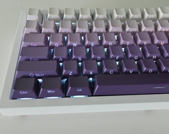 May include: A white mechanical keyboard with a purple gradient keycap set. The keys are labeled with the standard QWERTY layout and include function keys, number keys, and arrow keys. The keyboard has a white frame and a purple space bar.