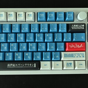 Op de afbeelding: Een wit en blauw toetsenbord met Japanse karakters en een rode en witte toets met de tekst "エヴァンゲリオン" (Evangelion). Het toetsenbord heeft een zwarte balk met de tekst "新世紀エヴァンゲリオン" (Neon Genesis Evangelion).