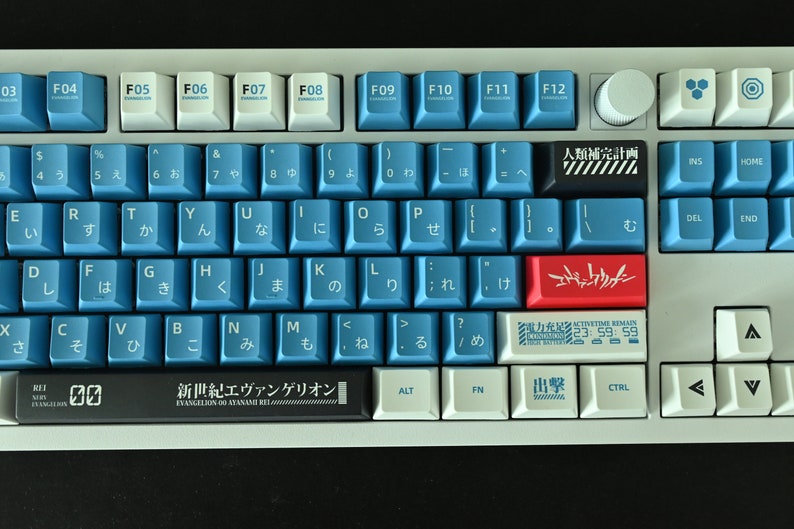 Op de afbeelding: Een wit en blauw toetsenbord met Japanse karakters en een rode en witte toets met de tekst "エヴァンゲリオン" (Evangelion). Het toetsenbord heeft een zwarte balk met de tekst "新世紀エヴァンゲリオン" (Neon Genesis Evangelion).