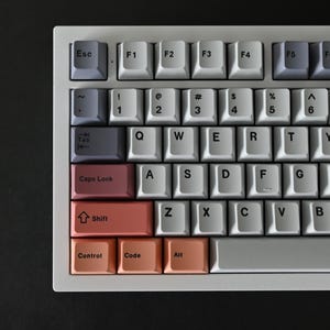 May include: A white mechanical keyboard with a gray, pink, and red color scheme. The keys have black lettering and the keyboard has a white frame.